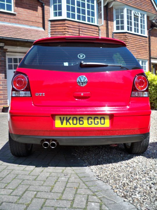 Pistonheads Polo Gti - The image features a red Volkswagen GTI parked on a driveway at the side of a house. The vehicle is positioned at an angle that showcases its rear side and back windshield. It has a shiny metallic emblem on the trunk lid. The car is surrounded by a neatly maintained brick driveway, and the house in the background has a white front door with a window above it. The car's license plate reads "VKO 6 GGO," indicating that the car is registered in the United Kingdom. There's no text other than the vehicle's license plate.