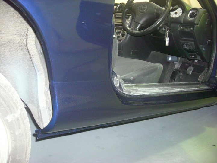 Rot in sills at rear wheel arches? - Page 1 - Mazda MX5/Eunos/Miata - PistonHeads - The image showcases the interior of an SUV or car, specifically focusing on the driver's side door opening. The car's blue interior can be seen. The seat is tucked into the car, revealing access to the footwell. The open door exposes some of the car's mechanical and electrical components, indicating possible maintenance or a freshly cleaned compartment. The shiny finish of the car door and the surrounding area reflect light, adding to the overall cleanliness of the car. The focus is on the interaction between the mechanical elements and the interior design of the car.