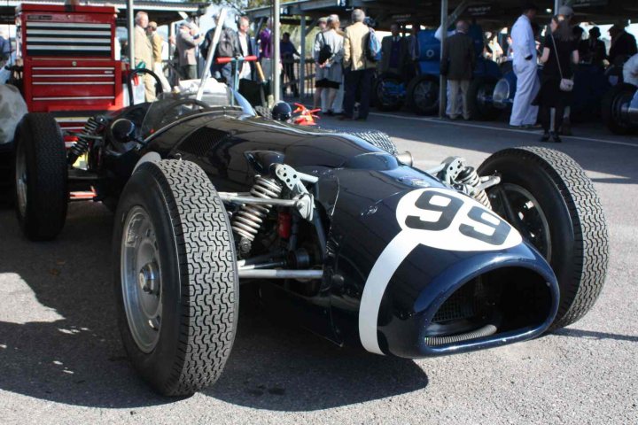 Revival images - Friday  - Page 1 - Goodwood Events - PistonHeads - The image features a sleek, black vintage race car parked amidst a crowd. The car is prominently displayed with the number 99 visible on its side. Its close proximity to the crowd suggests that it might be on display, possibly at an auto show or similar event. The color contrast between the dark blue of the car and the mostly grey and white tones of the crowd and background adds a striking element to the scene. The overall ambiance reflects a sense of nostalgia and admiration for the classic design of the race car.