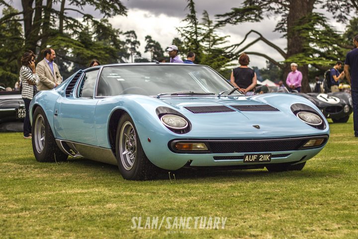 Countach  - Page 10 - Lamborghini Classics - PistonHeads - The image shows a vintage sports car, with a distinctive blue and white color scheme, parked on a grassy area, likely at a car show. There are several people in the vicinity of the car, appearing to be admiring or discussing it. The car is a two-seater, convertible with a long and narrow hood, which is characteristic of classic sports cars. The setting is outdoors, and the scene seems to convey a sense of leisure and appreciation for the automobile.