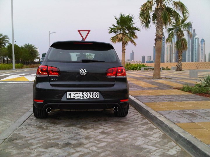 Pistonheads Bought Gti - The image features a modern black Volkswagen, parked on the right side of a paved overlook by the side of the road. The city skyline is visible in the background, suggesting this location is in an urban area. A neatly organized palm tree adds a touch of tropical exotica to the scene. The webcam appears to be mounted on a pole overlooking the area, capturing the skyline and the black car.