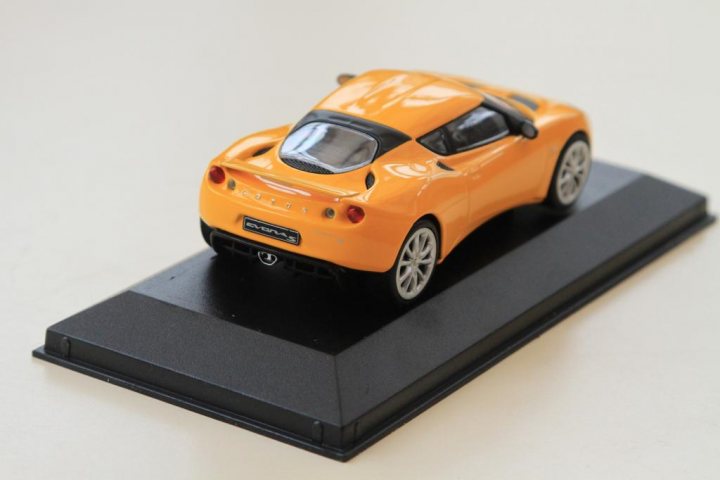 A close up of a red car on a motorcycle - Pistonheads - The image displays a vibrant, small-scale model of an orange high-performance sports car. The car is sleek and shiny, giving it a polished and aerodynamic appearance. It is presented on a black base, possibly a display stand, against a plain, light-colored background. The model's front and side elements indicate a compact and possibly vintage style, with a distinct sloping roofline and large, wide-angle headlights. The craftsmanship showcases attention to detail and a vivid color that stands out in the scene.