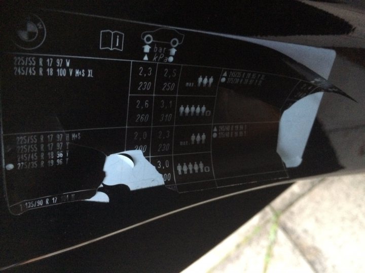 Optimium tyre pressure F10 on 19" - Page 1 - BMW General - PistonHeads - The image shows a detail of a vehicle, focusing on its door or window area which is partially torn or pulled back. The surface is reflective, and a large amount of text and numbers can be seen, likely pertaining to the vehicle's make, model, serial number, and possibly the result of a range of emissions tests such as carbon emissions, nitrous oxide emissions, or other environmental data. The text is densely packed, making it challenging to read every detail. The perspective is from a high angle, looking down towards the text, and the image has a black and white color palette.