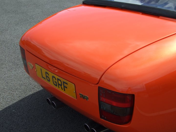 A red car is parked in a parking lot - Pistonheads - The image features a vibrant, gold-orange color accentuating the style of a compact car. The license plate reads "L6 GRF," printed in black font on an orange plate. The triangular shape of the license plate is characteristic of the region, UK, where the car is registered. The shiny surface and the reflective quality of the car's paint indicate it's well-maintained. The vehicle is parked on a gray asphalt surface under an unseen sky.