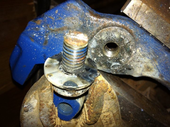 Removing sheared bolt - washer, welder and nut method - Page 1 - S Series - PistonHeads - The image displays a close-up view of a mechanical component. At the center, a metal bolt with a threaded shank can be seen against a blue surface, lubricated and dusty. To the left, a rusted component, possibly a brake liner or similar part, is attached with a single screw. Along the top edge, there is a marking with the word "Brock," suggesting the brand or model of the part. The background is dark and out of focus, indicated by blurred lines, which highlights the detail of the object in focus. The style of the image is a realistic photograph with a mild tilt, taken at an angle to show the components from above.