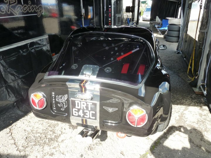 Spa 6 hours, 2015 - Page 1 - Classics - PistonHeads - The image captures a close-up view of a striking small car, parked in a garage with rows of tires visible in the background. The car stands out due to its black and white finish and distinctive triangular shapes on the rear. Each of these shapes contains a red light, adding a pop of color to the otherwise monochrome vehicle. The car's design, coupled with the unique color scheme, hints at a race car specification. Overall, the garage scene in the background provides a contrasting setting to the high-performance vibe of the car itself.