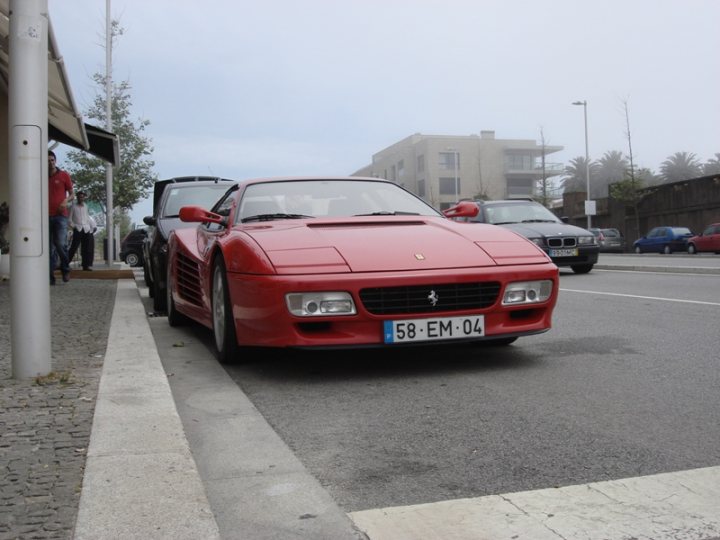 My 512TR - Page 1 - Ferrari V12 - PistonHeads - In the image, a striking red Ferrari sports car is parked by the side of a road. The license plate of the Ferrari reveals that it is from Germany. Behind the Ferrari, a few other vehicles are also parked neatly in a row. There are also a few people seen casually walking on the sidewalk, adding a human element to the scene. A tall building can be seen in the background, indicating that this location is likely urban or close to a city. The focus of the image, however, remains on the sleek and powerful Ferrari.