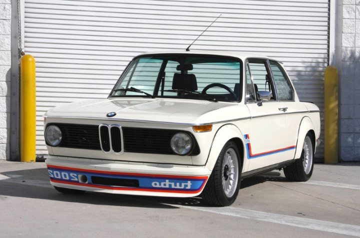 Your favourite car from the year you were born in... - Page 5 - General Gassing - PistonHeads - The image shows a white BMW parked in front of a closed garage door. The garage and the BMW door are parallel to each other. The BMW car is positioned at a slight angle, showcasing its front right wheel and side door. The vehicle is a two-door coupe with a compact design, and the image is taken during daylight, as indicated by the shadows on the ground.