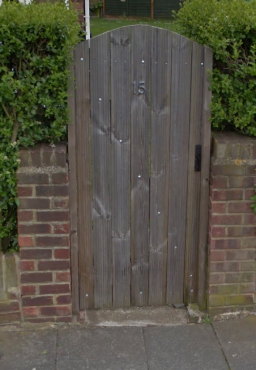 Anyone made a fence out of decking ? - Page 1 - Homes, Gardens and DIY - PistonHeads - The image portrays a tall, sturdy wooden gate that commands attention. The gate is set behind a row of closely packed bushes, their lush green leaves forming a vibrant contrast against the gate's wooden hues. The gate is numbered, the numerical '15' prominently marked at the top, suggesting it might be used to account for visitors or residents. The ground in the foreground is paved in a pattern that seems to be a mix of white and grey, leading up to the gate and inviting one towards the hidden location beyond. The style of the image is a simple, realistic photograph with no noticeable filters or alterations, giving it a straightforward, clear representation of the scene.