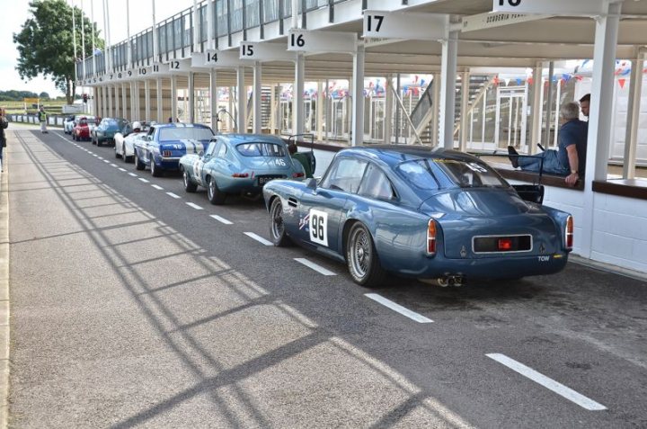 Supercar blokes: Mission Motorsport needs you! - Page 1 - Supercar General - PistonHeads - This image captures a vibrant scene at what appears to be a car show or a racing event. A line of vintage cars, predominantly painted in shades of blue, is parked neatly in a parking lot adjacent to a grandstand. The backdrop of the grandstand provides a stark contrast to the sleek, old-world charm of the cars.

In the foreground, we see a man perched on the back of the open-topped car in the center of the frame. His casual pose suggests an air of familiarity with the event and the cars. Other people are scattered throughout the scene, some near the cars, and others inside the grandstand, all seemingly engrossed in the spectacle that this car show or racing event is likely to offer.