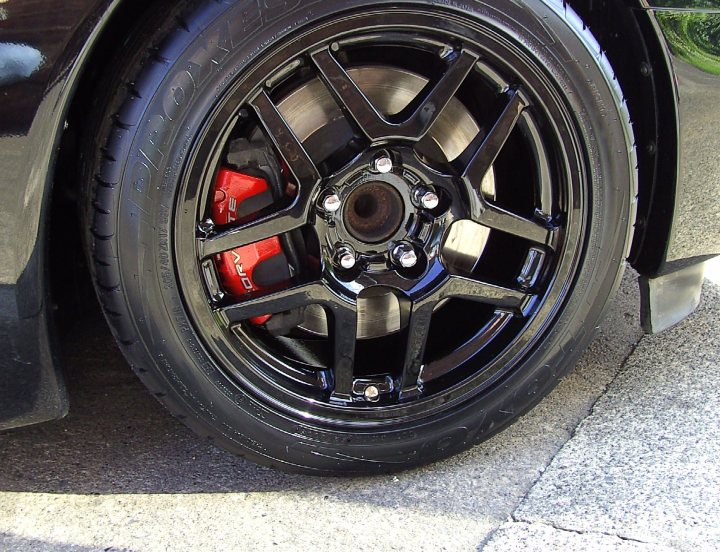 Chrome Refurb Pistonheads Wheel - The image focuses on a close-up of a tire and wheel on a vehicle. The tire is black and displays distinct tread patterns, typical for automotive use. The well of the wheel features a five-pointed star, a pattern often associated with owners' personalization. Inside the well, there is exposed hardware, including the wheel studs and wheel "keys," which securably lock the wheels to the vehicle. The wheel appears to be made of steel or a similar metal. The surrounding area looks like an asphalt road, possibly a driveway.