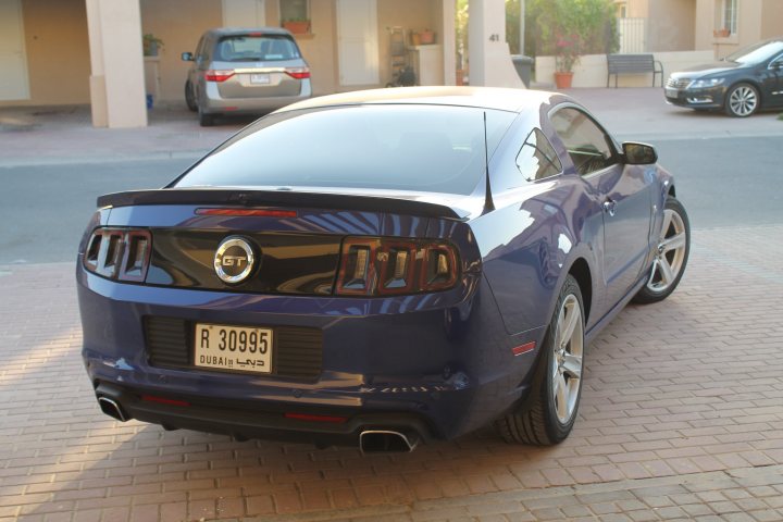 Sold the Golf, replaced with proper car - Page 1 - Middle East - PistonHeads - The image displays a blue Mustang car with the model year "R3095" on its license plate. It is parked in a parking lot next to a red brick area. There are other cars parked in the vicinity, with a beige car visible in the background on the left side. The car has two rear wheels visible in the image, and it appears to be an outdoor setting bathed in sunlight. There are no people visible in the scene.