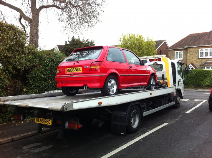 Fiesta RS Turbo Restoration - Page 13 - Ford - PistonHeads - In the image, a red hatchback car is being towed by a white tow truck. The car is securely fastened with straps on the back of the truck. The tow truck is parked on a street in a residential area, with houses visible in the background. The white lines on the road indicate parking restrictions or no-parking zones. The scene suggests that the car might be experiencing some mechanical issues and requires a tow to reach a repair shop.