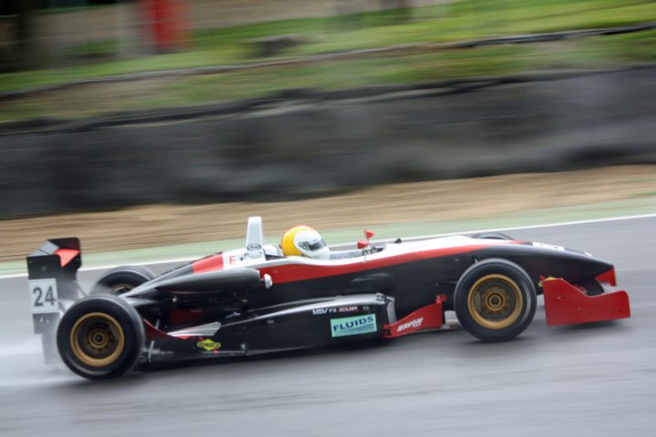 Pistonheads - The image captures a thrilling moment of the Formula 1 race. A Formula 1 car, painted in striking shades of black and orange, is distorting the ground beneath it with its high-speed motion. The car, numbering 24, is positioned in the lower right quadrant of the image. The surrounding environment is a blur of colors, predominantly green and brown, indicating a race track during an autumn season. This image encapsulates the adrenaline and speed that are synonymous with Formula 1 racing.