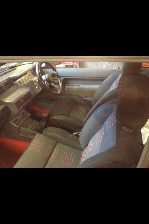 Renault 5 GT Turbo Wanted - Page 1 - French Bred - PistonHeads - The image shows an interior view from the back seat of a car. The seats are a dark upholstery with visible headrests. The floor mat appears to have a patterned design in red. The steering wheel is visible to the left of the image. The quality of the image is not high, due to its brightness and distortion, making fine details difficult to discern. The car seems to be in motion, as indicated by the blurred lower edge of the image, suggesting a dynamic motion, likely taken from a moving vehicle.