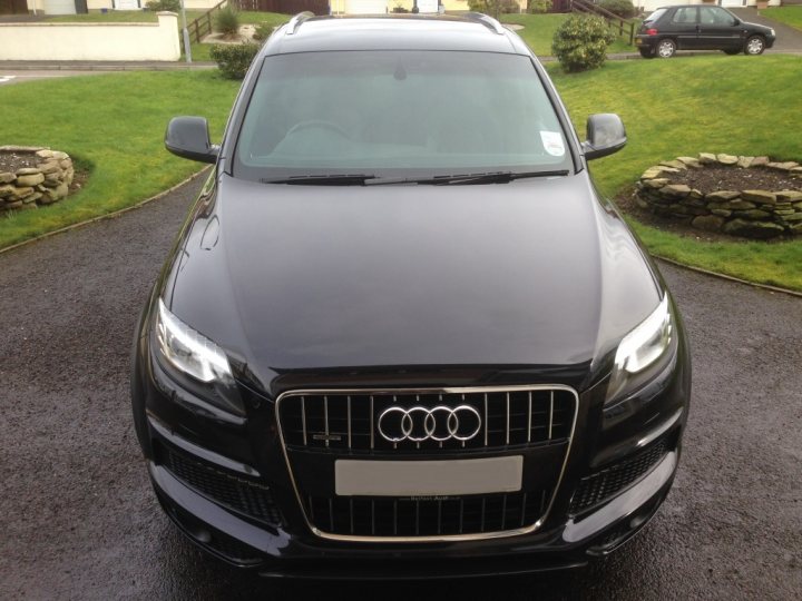 Show us your FRONT END! - Page 102 - Readers' Cars - PistonHeads - The image presents a close-up view of a sleek, black Audi parked on an asphalt driveway. The car's size and smooth lines are prominent, suggesting it might be a larger model. The car is parked near a curb, giving the impression that it is stationed away from the house entrance. The background is lightly blurred, drawing focus to the Audi car, but there are signs of a suburban setting with a house and a car parked in the distance.