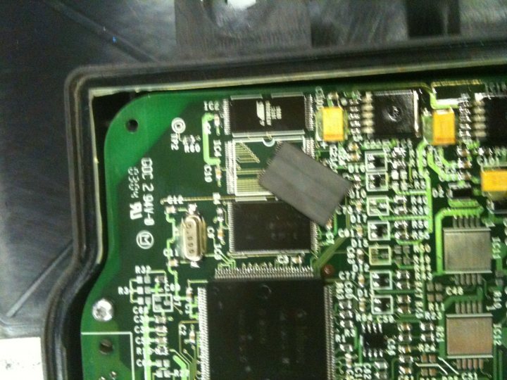 Pistonheads Layup Misfire Month - The image presents an upward view of an electronic circuit board. A prominent feature in the center is a rectangular, black integrated circuit (IC) packaging. This IC is surrounded by a matrix of green circuit lines, and adjacent to it is a small metal PCB pad. The circuit board, visible in shades of green and white, exhibits complexity with numerous connections and layouts indicative of advanced electronics design.