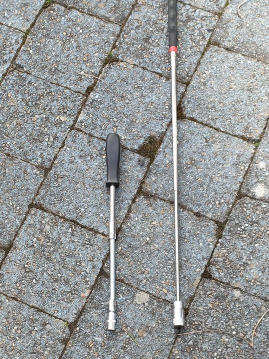 Pistonheads - The image shows a pair of golf clubs lying on their sides on what appears to be a paved surface. One club has a red head while the other is silver, and both have black shafts. There's also an unusual object next to the clubs; it looks like a pair of scissors with a long handle, but it's not clear what its purpose is in relation to golf clubs. The scissors are open with the blades facing each other. The background is blurred, making it difficult to discern any specific details about the setting.