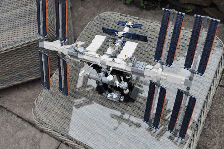 Non Technic LEGO - Page 280 - Scale Models - PistonHeads - The image shows a model of the International Space Station (ISS) with several modules attached to it. The ISS is placed on top of a table. There are no people present in the image. The setting appears to be an outdoor environment, indicated by natural light and a brick surface in the background.