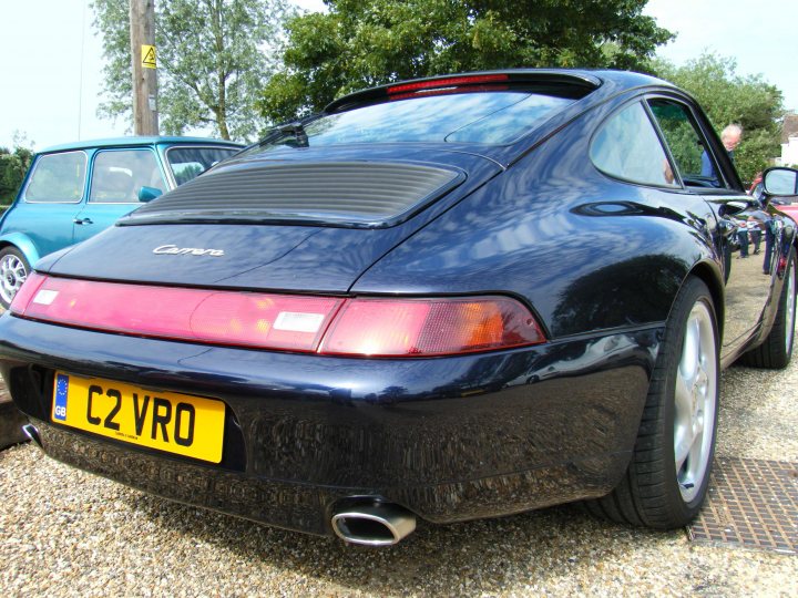 Breakfast Meeting, The Hare, Roxwell 4th June - Page 1 - Kent & Essex - PistonHeads - The image features a classic blue Porsche car parked on a gravel driveway. The vehicle is positioned at an angle, showcasing its distinctive design elements, including the iconic rearengine spoiler. The car bears a yellow license plate with the text "C2 VRO" and has a visible exhaust pipe on the right side of the rear. The setting includes a tall wooden power pole and a few unidentifiable objects in the background. Another car, which appears to be a light blue compact vehicle, is parked nearby. The image conveys a sense of nostalgia for vintage automobiles.