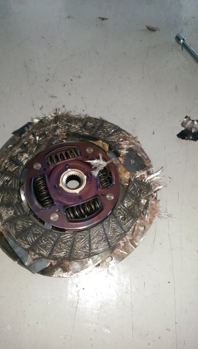 Toyota Gt86 Clutch destroyed - Page 1 - Jap Chat - PistonHeads - The image shows a dirty, broken car hubcap, which appears to be a bronze or red color, with visible wear and mechanical parts, such as springs, exposed on its surface. It is lying on a grey surface, with a small metal piece nearby. The hubcap looks like it has been damaged or removed from a vehicle, possibly due to an accident or maintenance. The scene suggests a mechanical or repair setting.