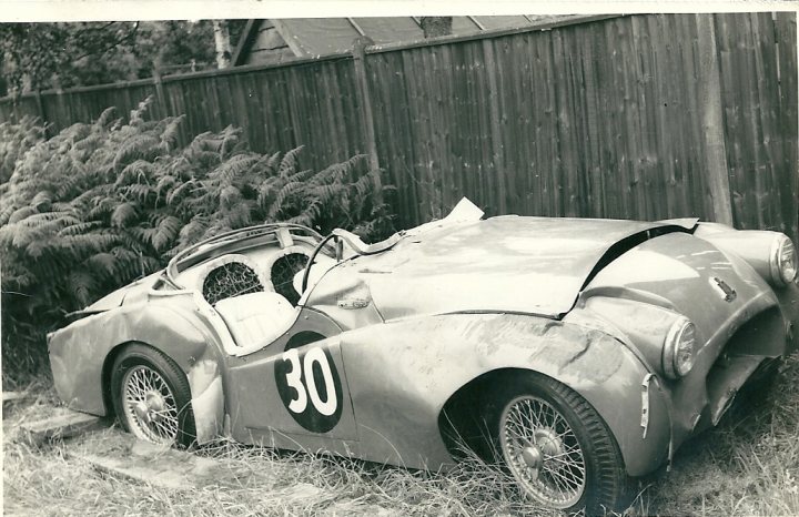 Before after rebuilds - Page 8 - Classic Cars and Yesterday's Heroes - PistonHeads - This is a black and white photograph featuring a vintage car that is in a highly damaged condition. The car is resting on its side, suggesting it has been involved in a significant accident. The photo appears to be older, with aged characteristics typical for photographs from the past half-century. The car is labeled with the number "30," and its overall appearance, including the state of its body and wheels, indicates that it is in the process of recovery from the crash aftermath. The car is parked next to a wooden fence and there are trees visible in the background.