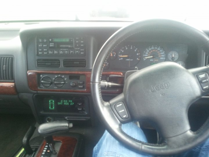 My winter snotter..... Do you have yours yet?  - Page 1 - Readers' Cars - PistonHeads - The image shows the interior of a car, focusing on the dashboard and steering wheel. The steering wheel is black and prominently displays the brand "Jeep" in white lettering in the center. Various dials and indicators are visible on the dashboard, including a speedometer, tachometer, and air conditioning controls. The perspective of the shot appears to be from the passenger side, with a glimpse of a person's leg visible in the bottom right corner, suggesting they are behind the steering wheel. The overall style of the dashboard has a somewhat dated look, with a dark color scheme and physical buttons and knobs for control.