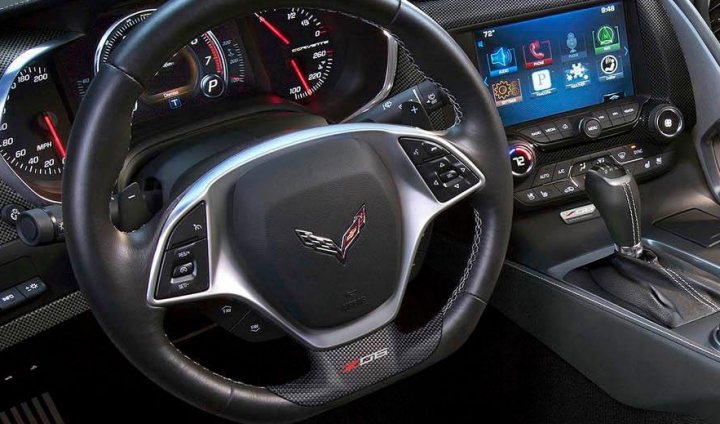 C7 Z06  - Page 1 - Corvettes - PistonHeads - The image captures a close-up view of the dashboard and steering wheel inside a modern vehicle. The steering wheel, prominently featuring the Cadillac logo, is black with silver accents and numerous buttons for controlling infotainment and driver assistance systems. The dashboard showcases multiple gauge displays and digital interfaces, indicative of advanced technology options, such as GPS navigation and smartphone integration. The overall presentation of the car's interior is sleek and modern, enhancing the sense of luxury and advanced functionality found in top-tier vehicles.