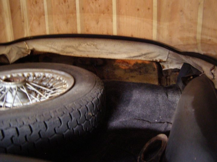 Early TVR Pictures - Page 73 - Classics - PistonHeads - In the confinement of a rusted car trunk, a spare tire and a shoe box share the space, both marked by the passage of time. The tire, with its textured tread, is a silent witness to the stories of journeys undertaken. Adjacent to it, a shoe box waits, its contents hidden within its confines. The dirt floor beneath them hints at the rough winter months. This image captures a moment frozen in time, within the cramped space of a backseat of a car.