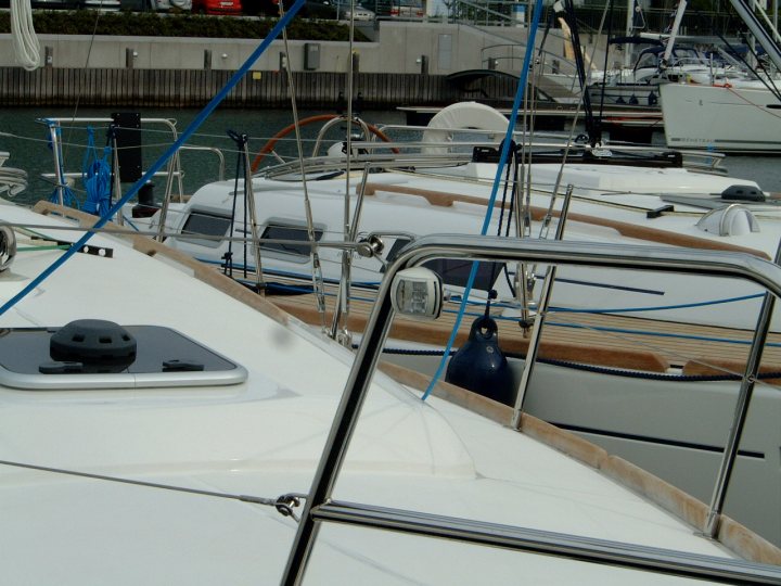 The image captures a serene harbor scene with several boats, predominantly white. The boat closest to the camera is distinctive with its black outboard motor and a blue canister on the deck. The other boats in the background also have sleek designs and white hulls, creating a harmonious maritime aesthetic. The vantage point is particularly interesting, as it appears to be taken from the deck of a boat, providing a perspective that emphasizes the fellow vessels and the surrounding water. The overall scene evokes a sense of calm and tranquility, typical of a harbor setting.