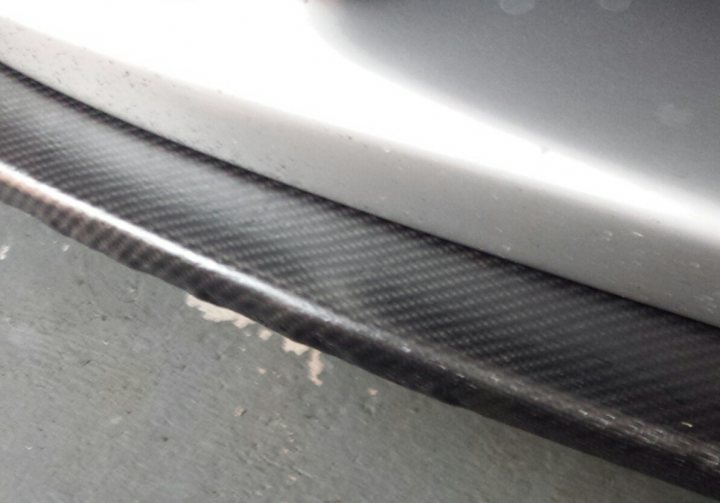 A large metal oven sitting on top of a wooden platform - Pistonheads - The photograph focuses on a section of a car's bodywork, likely near a front door vent. The metal is matte, reflecting a pattern consisting of straight and wavy lines, which is characteristic of carbon fiber impregnation or perhaps a vinyl wrap designed to resemble it. The underside of a flap or panel, full of these lines, reveals signs of wear and accumulated fluff or debris. The orientation of the image is horizontal, capturing a close-up view of the vehicle's lower awkward edge, and the backdrop fades into darkness.