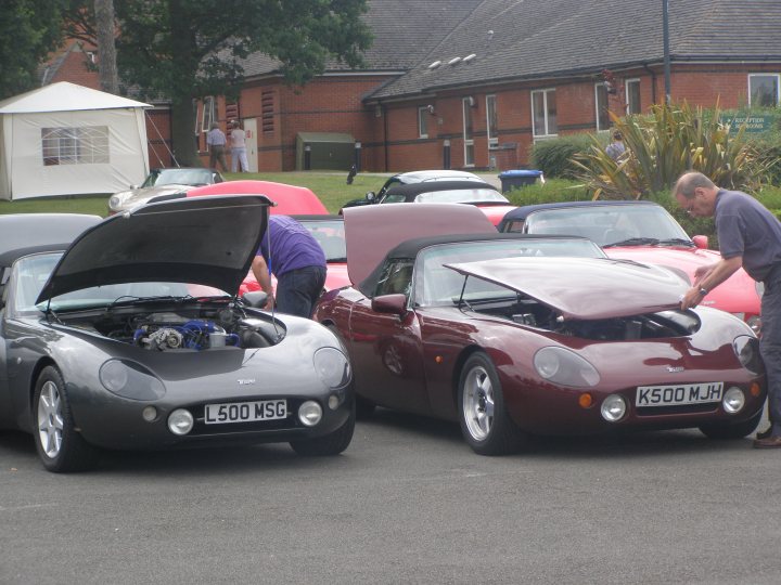 Griff Pistonheads Growl - The image depicts a parking lot where three convertible sports cars are parked side by side, with the hoods of two of them open. Two people are standing near the car with the hood open, engaged in some sort of activity involving the cars. The cars are of different models and colors, suggesting they might be used for racing or performance. It is a daytime scene, and there's a person standing near the back of the parking lot.