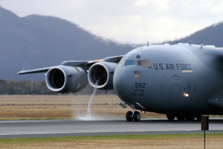 Farnborough Air Show 2016 - Page 12 - Boats, Planes & Trains - PistonHeads - This image shows a large gray military aircraft on an air strip. The plane, labeled with "US AIR FORCE" and a serial number (5162), has a dual-screw-rider design. It is emitting a plume of water, possibly engine cooling or spraying, which fogs the air slightly around it. The aircraft is positioned on the runway, ready for takeoff or having just landed, surrounded by a verdant landscape with what appears to be a mountain in the distance. The sky is overcast, contributing to the mist in the air.