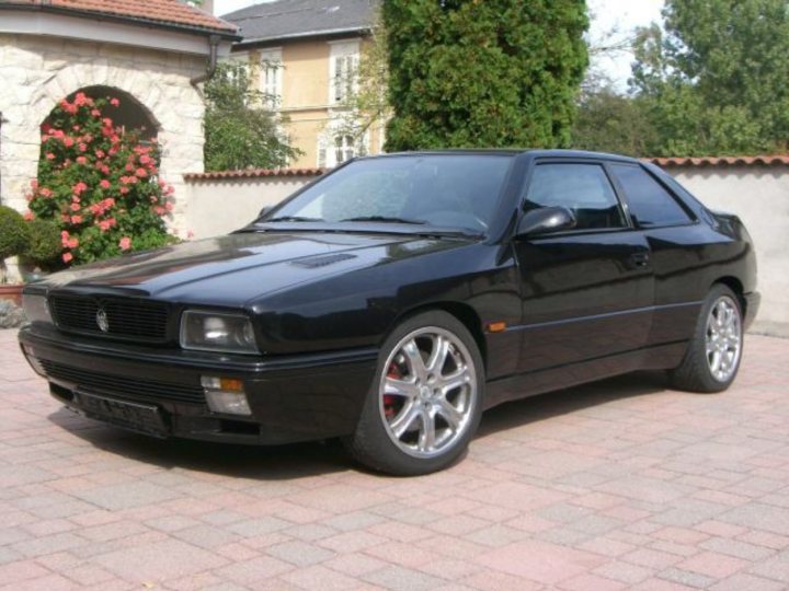 RE: Spotted: Opel Manta i200/i400 - Page 5 - General Gassing - PistonHeads - The image features a sleek, black coupe parked on a brick driveway. The vehicle is positioned against a backdrop that includes a stone wall, garden roses, and an old house with ivy. The car's glossy finish and silver rims give it an elegant appearance. The design of the car suggests that it's a sports or performance model, possibly intended for spirited driving or, given its aesthetic, for a polished and professional image.