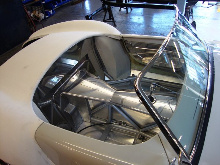 A close up of a motorcycle parked in a garage - Pistonheads - This image shows the interior of a vehicle's engine compartment, viewed from the cabin. The light-colored paint suggests a clean, well-maintained vehicle. The metal structures and geometric shapes indicate the complexity and precision of automotive engineering. There's a clear visual contrast generated by the metal components reflecting light. A power tool, likely a drill, rests nearby, hinting at a repair, modification, or routine maintenance process. Overall, it's a detailed snapshot of a car's mechanical heart.