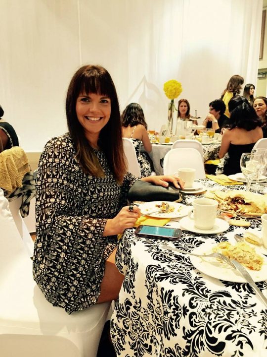 A woman and a man are cutting a cake - The image features a woman sitting at a table with a meal in front of her. She appears to be enjoying the food and is posing for the camera, smiling brightly. Behind her, there's another person seated at the same table, also partaking in the meal. The setting suggests a formal or semi-formal event, as indicated by the tablecloth and the presence of what looks like a wedding cake on a nearby table.