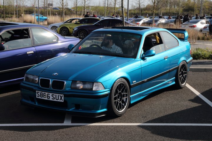 M3 CSL and M5 - Page 6 - Readers' Cars - PistonHeads UK - The image depicts a vibrant scene in a parking lot. Dominating the frame is a striking blue BMW, parked in front of a silver sedan. The BMW, characterized by its sleek design and white license plate reading "S90", exudes an air of luxury and performance. It's not just any BMW; it's a race car with modifications like a roll cage and large rear wing.

A person is standing next to the BMW, seemingly engaged in conversation or admiring the vehicle. The background of the image reveals other cars parked further back, adding depth to the scene. The concrete surface beneath them suggests they're in an urban environment or possibly at a car show.