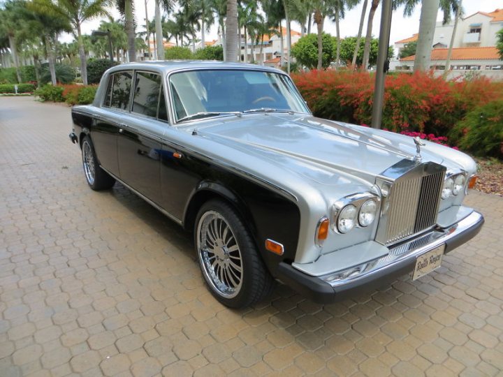 Silver Shadow Alloys... - Page 1 - Rolls Royce & Bentley - PistonHeads - The image shows a classical car parked on what appears to be a brick-paved driveway. The car has a chrome-colored grille and sleek silver exterior, giving it a vintage look. It features white-wall tires and a coated conversion for a convertible top, which is likely located at the center of the car during open-top use. The setting is a well-maintained outdoor area with manicured greenery and a clear sky in the background.