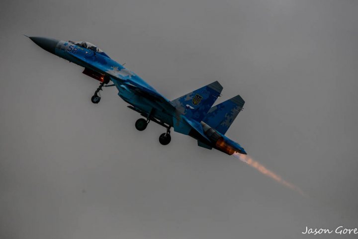 RIAT 2017 - Page 4 - Boats, Planes & Trains - PistonHeads - The image shows a fighter jet soaring through an overcast sky. The jet is blue with patterns on it, moving from the bottom to the top right of the frame. The plane is captured mid-flight, its nose pointed upward, and it leaves a contrail behind it, suggesting its speed. The background is a uniform gray, punctuated by the jet's vibrant color and the condensing trail it leaves.