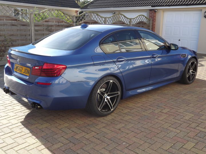 Is the f10 M5 a fun car? - Page 2 - M Power - PistonHeads - The image showcases a dark blue BMW car parked on a driveway in front of a house. The car appears to be in good condition with tinted windows and alloy wheels. The driveway is paved with interlocking brick pavers, adding a touch of elegance to the scene. The house in the background features white siding and a black roof, complementing the overall aesthetic of the image. The sky is overcast, casting a soft, diffused light over the car and its surroundings.