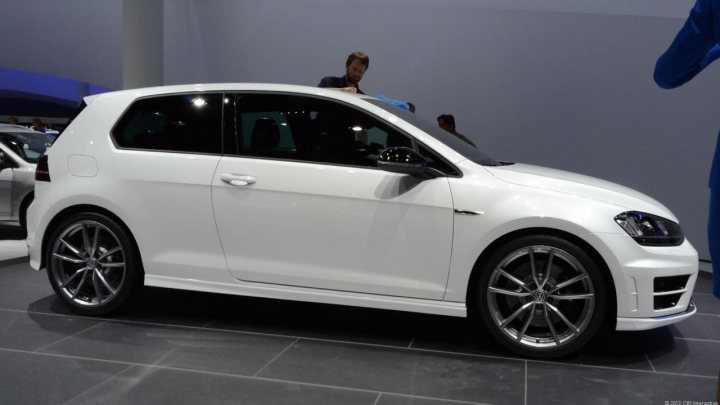 A car with a surfboard strapped to the back - Pistonheads - The image displays a modern, white, four-door sedan car with a distinct, sporty design, positioned in an indoor setting with a gray tiled floor. There is a reflection visible in the car's shiny side, showing a few people behind it but without explicitly revealing any specific activities they might be engaged in. The vehicle might be displayed at an auto show or a showroom, as suggested by the portant context, and the lighting enhances the car's features and the setting's cleanliness.