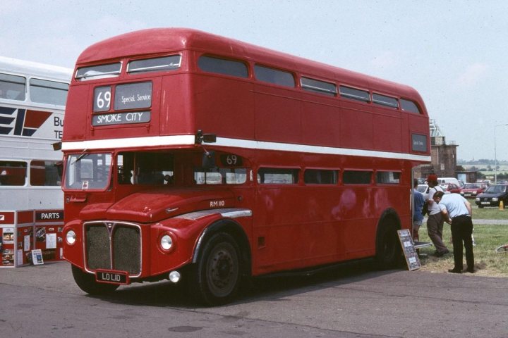 Pistonheads - In the image, a prominent red double-decker bus is parked in a lot. The bus is mostly solid red with a few white accents on the lower deck. The bus bears the number 69 and is parked in front of the registration number 9, and 5, suggesting it might be for display or out of order.

Several people are gathered around the bus, possibly admiring its design or discussing something related to the bus. Behind the bus, there is another, smaller vehicle, which could also be of interest to people in the lot.

A large expanse of green brings a natural touch to the scene, contrasting with the red bus and the pavement. The lot itself is fairly busy, indicating that it might be a public transportation hub or a popular attraction.