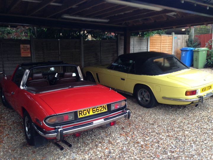 A car that is parked next to a fire hydrant - Pistonheads - In the image, an outdoor setting is captured, with two vintage cars parked under a wooden carport. The older model red car with a yellow license plate is positioned on the left. On the right, a yellow car with a black license plate is parked. The background reveals a blue recycling bin, signifying some effort towards environmental sustainability.