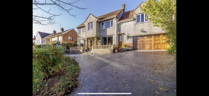 Layout / Renovation Ideas - Page 1 - Homes, Gardens and DIY - PistonHeads - The image shows a two-story house with a pitched roof. It has white walls and features a garage door on the left side. There are two visible windows, one on each level of the home. The driveway is made of gravel, and there's a tree next to the entrance. A portion of a brick wall can be seen in the foreground. The sky is clear, suggesting good weather.