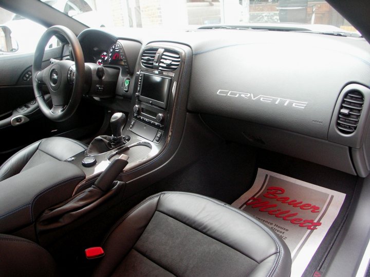 How about some ZR-1 photos to cheer you up? - Page 1 - Corvettes - PistonHeads - The image showcases the inside of a gray Corvette car, demonstrating the stylish interior. The car is equipped with a steering wheel on the left side of the dashboard, and the prominent Corvette insignia is visible in the glove box. The black leather seats, positioned for a driver, provide a sense of luxury. On the floor mat in front of the car, there's an advertisement for 'Bauer Krause' written in red letters, indicating a possible upgrade or themed setup.