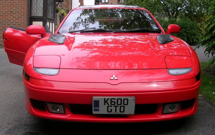 Pistonheads - The image shows a vibrant red sports car parked on what appears to be a residential street. The car features a sleek design with a prominent step between the doors and the cabin. The brand name of the car, which is a Mitsubishi, is visible on the front of the vehicle. The license plate of the car reads "K600 GTO," indicating a registration boldly. The car is parked neatly along the pavement, next to a brick wall. The overall condition of the car suggests it is well-maintained and possibly belonging to someone who takes great pride in their vehicle.