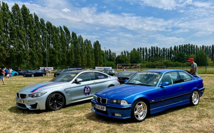 Pistonheads - The image shows an outdoor event with cars on display. There are two distinct cars: a blue BMW with a sunroof and a white sports car, both parked next to each other on grass. In the background, there are trees providing a natural backdrop. The focus of the image is on these vehicles, suggesting that they might be the main attraction or subjects of interest at this event.