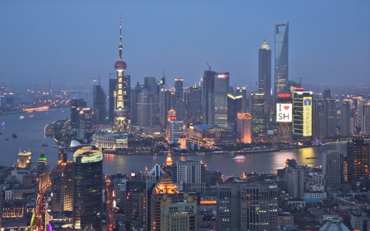 Pistonheads - This image captures a stunning nightscape of Shanghai, China, with its city skyline illuminated against a deep blue sky. The city is encircled by the Huangpu River on which a fleet of ships Add majesty to the view. Multiple skyscrapers, including the Jin Mao Tower and Shanghai World Financial Center, punctuate the skyline, casting their distinct lights that are reflected on the waters below.