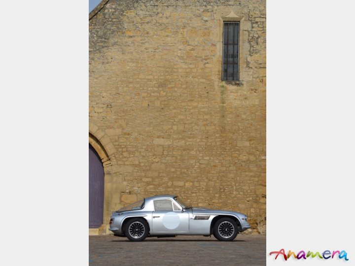 Early TVR Pictures - Page 36 - Classics - PistonHeads - The image features a silver sports car parked next to a stone building. The car is positioned in front of the building, slightly angled towards the camera. The stone building has a tall, narrow window on the right side, which adds a sense of height and stature to the structure. The background is clear, with the focus primarily on the car and the building, giving the scene a clean and minimalistic aesthetic.