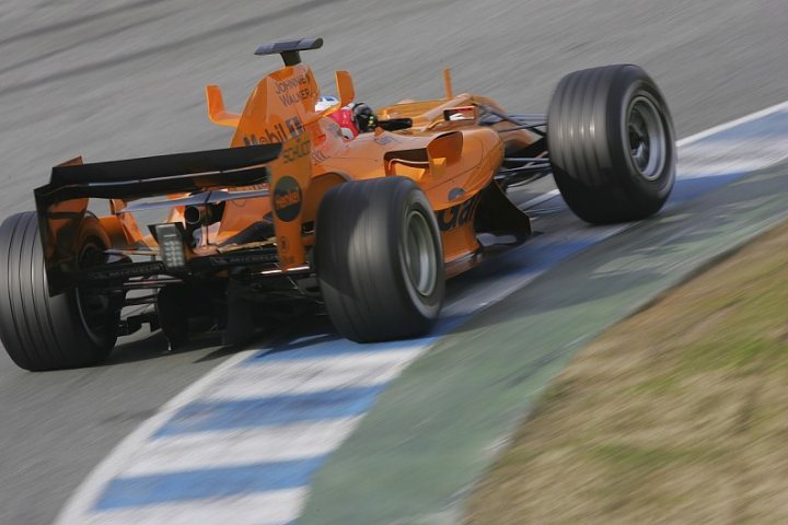 McLaren F1 2017 - Page 1 - Formula 1 - PistonHeads - The image depicts an orange Formula 1 car, heavily detailed with advertisements, making a turn on a race track. The track exhibits a blue and white striped pattern, curving to the right in the foreground. The car is tilted to the left, indicating the centrifugal force experienced during the turn. The rear wings and tires suggest high speed. The setting and the sports topic enable to identify this as a racing event.